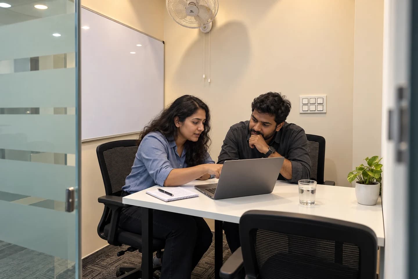 AI-generated office scene: two colleagues reviewing one laptop together